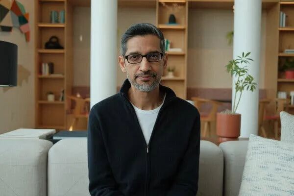 Sundar Pichai sits on a beige couch and stares straight into the camera.